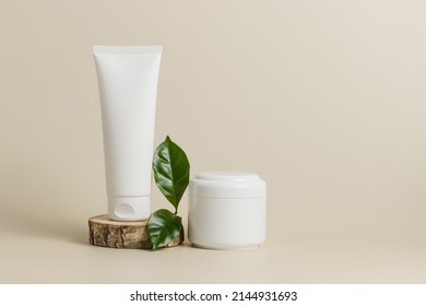 Mockup unbranded tube face cream on wooden stand with cream bottle and green leaf, organic cosmetic, pastel background, copy space