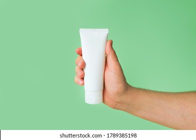 Mockup Of Unbranded White Bottle Tube For Branding And Label And Male Hand On A Green Background. Shaving Foam Or Male Skin Care Concept. Minimalism.