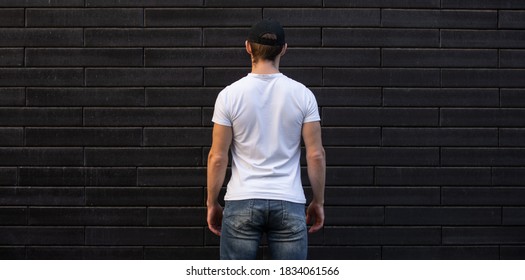 Mockup of unrecognizable man in empty white t-shirt standing against brick wall, back view