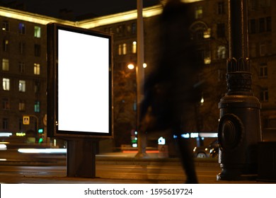 Mockup Vertical Billboard Standing In City City Format. Glowing At Night Billboard With An Advertising Field. With Blurry Cars Driving By And People Walking