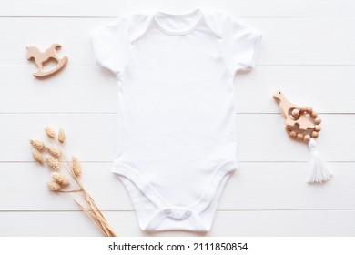 Mockup Of White Baby Bodysuit On Wood Background With Dried Flowers And Toys, Flat Lay. Blank Baby Clothes Template In Neutral Color.