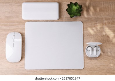 Mockup of white blank computer mouse pad or mat with props, mouse, earphones and power bank on table. Modern gadgets. Top view. Flat lay