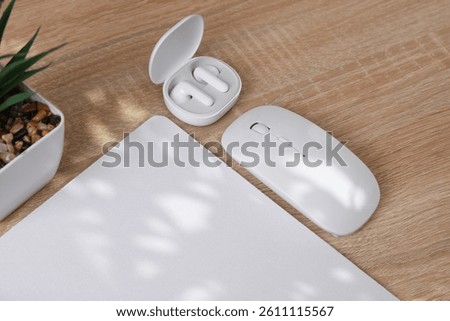 Mockup of white blank computer mouse pad or mat with props, mouse and earphones on table. Top view.