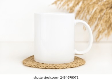 Mockup of white mug on table with jute coaster and dried flowers. Blank 11 oz ceramic coffee cup mock up in Boho style, neutral color.