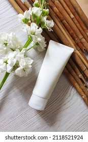 Mockup of white squeeze bottle plastic tube for branding of medicine or cosmetics - cream, gel, skincare. Cosmetic bottle container, matthiola flowers and reeds on wooden table.