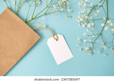 A mock-up of a white tag, a label and a price tag near a craft bag with flowers lie on a blue table. Empty space for text. Close-up - Powered by Shutterstock