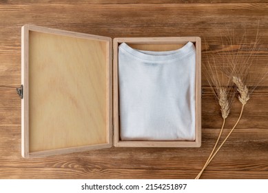 Mock-up of a white T-shirt inside a wooden box on a dark wooden table and some ears of wheat