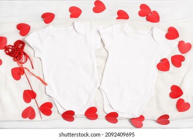 Mockup white mockup twins baby body suit decorated garland of red paper hearts. Happy Valentines Day baby apparel flatlay on white wood background, flat lay, top view, copyspace.