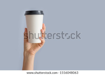 Mockup of woman hand holding up a Coffee paper cup isolated on grey background. Front view