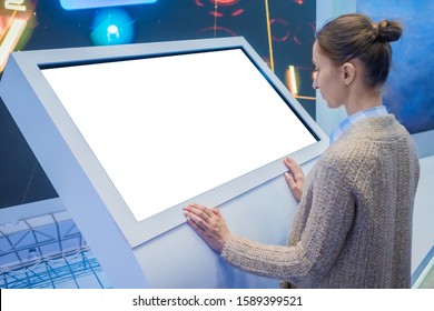 Mockup: woman looking at blank white interactive touchscreen display of electronic kiosk at technology exhibition, museum. Mock up, copyspace, template, isolated, white screen, futuristic concept