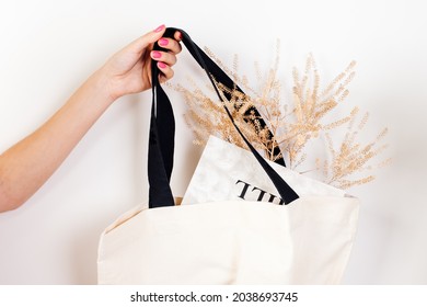  Mockup of woman's hand holding reusable white cotton eco-bag with black handles with dry flowers and newspaper lying in it on white isolated background for text or design, concept of zero waste. 