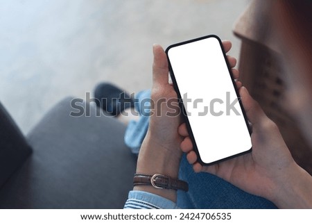 Mockup, woman's hands holding mobile phone with blank screen in coffee shop. Woman using smartphone, looking at the screen, over shoulder view