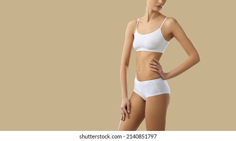 Model with beautiful fit slim body posing in comfy white underwear. Cropped shot of young woman wearing basic set of soft bra and underpants standing isolated on blank beige text copyspace background