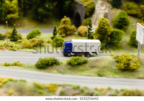 Model or model of a blue truck with a white\
van-body goes on the road rural landscape. Model truck on the\
asphalt road. The effect of tilt\
shift