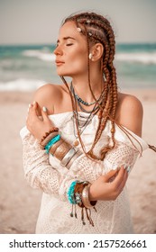 Model in boho style in a white long dress and silver jewelry on the beach. Her hair is braided, and there are many bracelets on her arms. - Shutterstock ID 2157526661