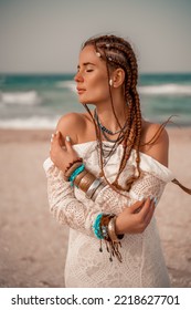 Model in boho style in a white long dress and silver jewelry on the beach. Her hair is braided, and there are many bracelets on her arms.