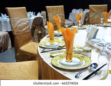 Model Of Chinese Set Table Equipment Arrange On Round Table With Lazy Susan Set On Mirror, Setting Up With Golden Chinaware, Golden Cloth Napkin, Silverware Spoon & Chopsticks, Golden Cover Chairs. 