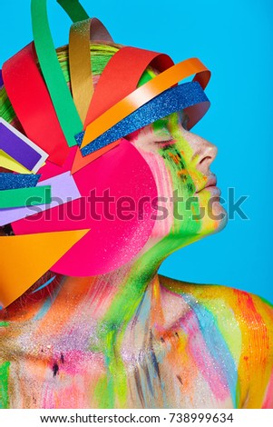 Model with colorful abstract makeup in multicolored helmet on blue background.