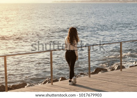 Model of curly curly hair being photographed on a pier in the sea at sunset