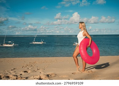 Model holds a pink float while walking along the sand