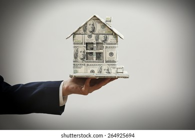 Model of house made of money in male hand on gray background