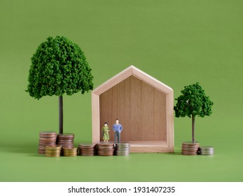 Model house with miniature people and coins on green background. Space for text