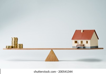 Model House And Money Coins Balancing On A Seesaw