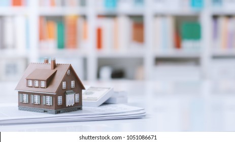 Model house, paperwork and cash money on a desktop: real estate, home loan and investments concept