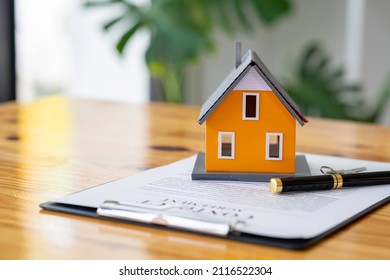 Model houses and contract documents on the desk in the office to decide to sign a home insurance contract about mortgage and home insurance offers - Shutterstock ID 2116522304