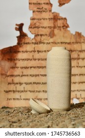 A Model Of A Jar Used For The Dead Sea Scrolls Against A Blurred Background Of The Isaiah Scroll