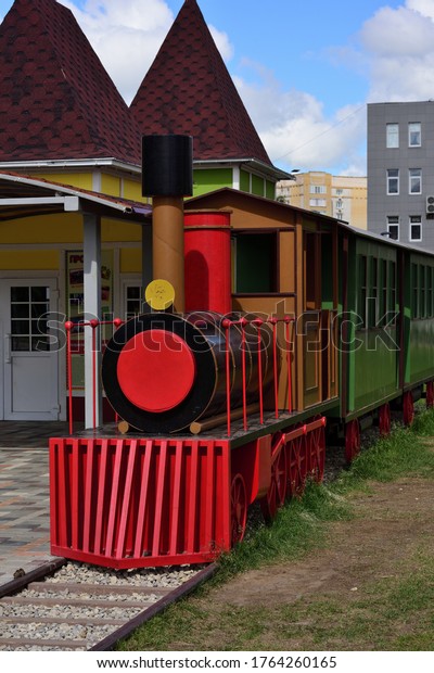 A model of a locomotive made of wood, painted\
in bright color in a city park. Door advertising : Bicycle, gyro\
scooter and electric car\
rental