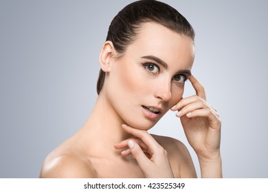 Model looking at camera and smiling surprisingly. Touching chin and temples. Wearing pigtail, nice make-up. Beauty portrait, head and shoulders. Indoor, studio - Shutterstock ID 423525349