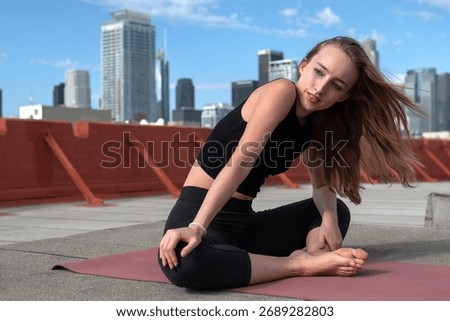 A model performs an elegant yoga sitting pose on a rooftop, showcasing serenity and mindfulness against a stunning city view, ideal for wellness, fitness, and lifestyle imagery.