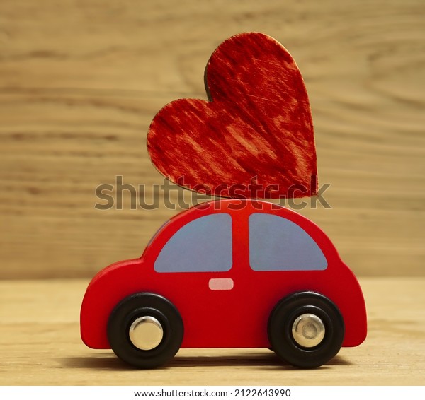 model of pink car with red heart on the roof on\
wooden board background. car toy with a heart on the roof on wood\
backdrop. Valentines Day\
card.