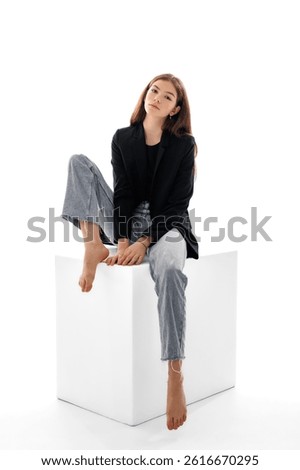 Model poses elegantly on a white cube wearing casual attire in a studio during a photoshoot