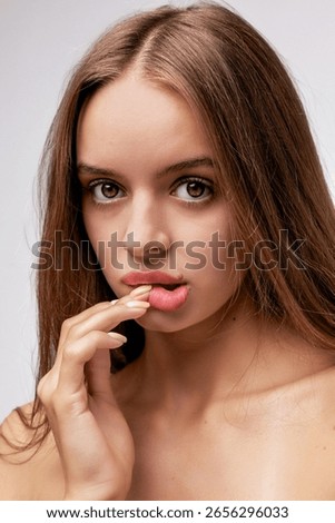 Model poses with an enticing expression while gently biting her finger in studio lighting