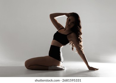 Model poses gracefully in studio while kneeling on soft surface showcasing elegant silhouette