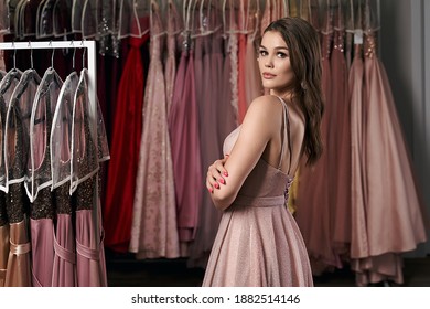 Model Selecting An Outfit For Occasion In Dress Hire Service With Many Options On Background.