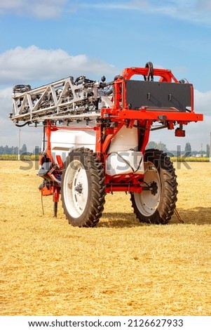 Model of a trailed sprayer with a high wheelbase against the background of a harvested wheat field on a sunny day in a folded transport state. Vertical image.