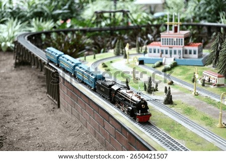 Model train set in a garden setting featuring a miniature locomotive and buildings, showcasing intricate details and vibrant colors.