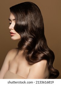 Model Waves Hairstyle. Brunette Beauty with Smooth Hollywood Curls. Woman with Shiny Wavy Hair and Nude Make up over Beige Background