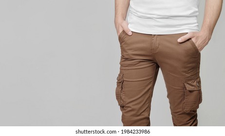 Model Wearing Brown Cargo Pants With Hands In Pockets On Grey Background, Empty Place For Text On The Left. Mockup, Template.