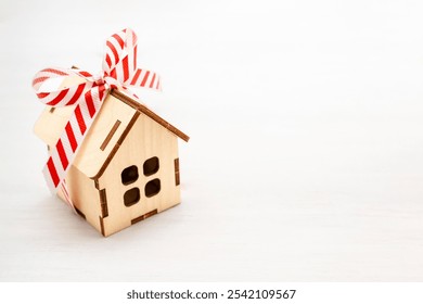 Model wooden house with a tied bow made of wrapping white red ribbon on a light wooden table close-up, background with copy space. Gift, present, buying a new house, mortgage, real estate concept. - Powered by Shutterstock