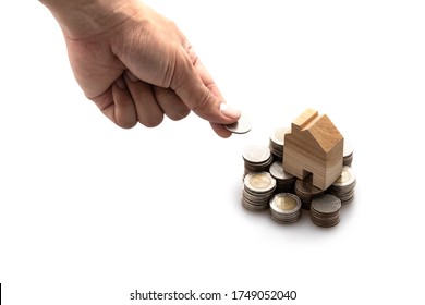Modeled wooden house placed on a stack of coins arranged in a row And the man's left hand is placing a coin Isolated on white background and copy space, saving and investment concept