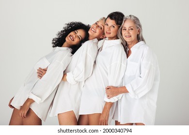 Models Of Different Ages Embracing Their Natural And Aging Bodies In A Studio. Four Confident And Happy Women Smiling Cheerfully While Wearing Mens Shirts Against A White Background.