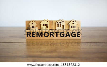Models of a wooden house. Word 'remortgage' on wooden block. Copy space. Business concept. Beautiful wooden table, white background.