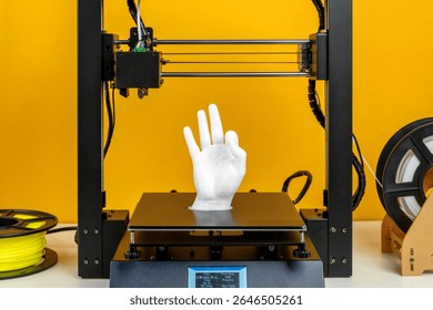 Modern 3D printer creating white plastic hand model, advanced additive manufacturing process with filament reel, yellow background, symbol of innovation, prototyping, technology development, future