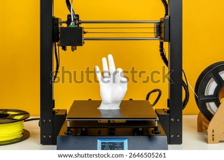 Modern 3D printer creating white plastic hand model, advanced additive manufacturing process with filament reel, yellow background, symbol of innovation, prototyping, technology development, future