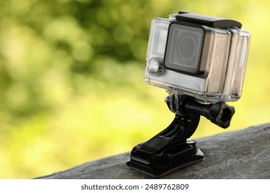Modern action camera with mount on wooden surface outdoors, closeup. Space for text