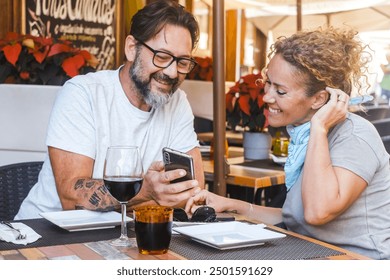 Modern adult couple sitting at table restaurant watching smartphone to leave a review feedback after lunch. Choosing the best pizzeria before eat reading comments on line on website on the phone - Powered by Shutterstock